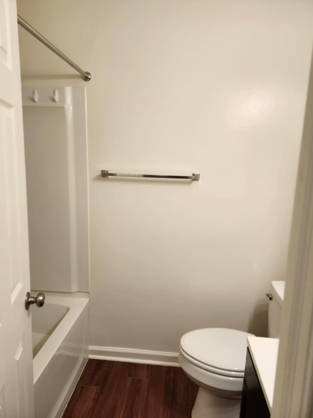 A bathroom at Calvertowne with a white tub and shower surround, a towel bar, and dark wood-look plank flooring