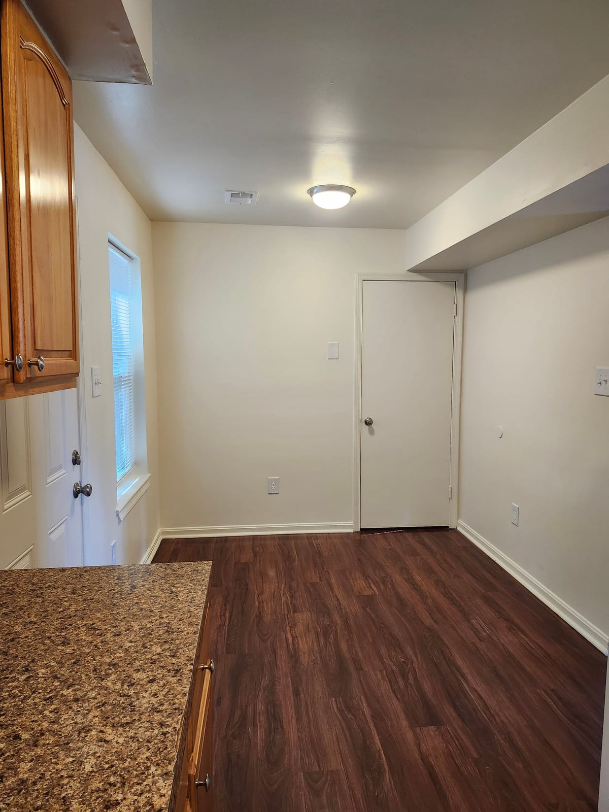 A dining space beside the kitchen at Calvertowne, with a window, a white door, and dark wood-look plank flooring