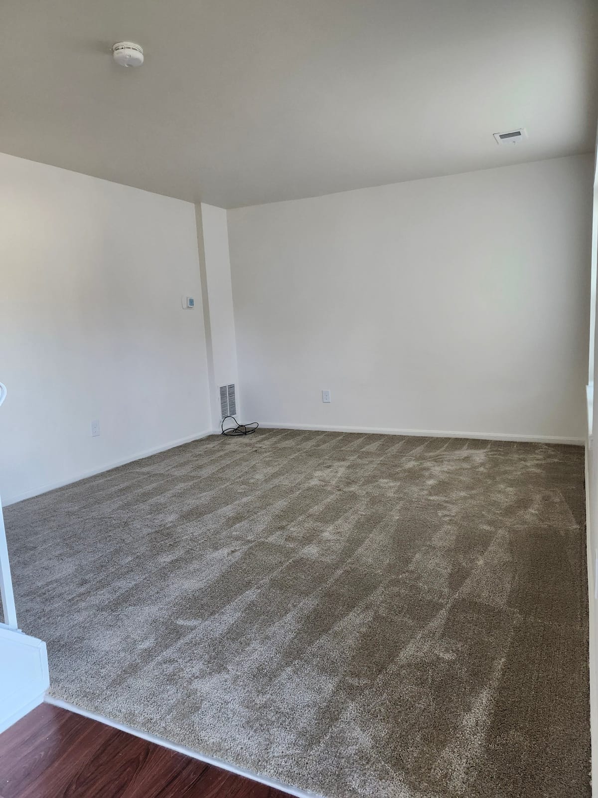 A living room at Calvertowne with freshly vacuumed wall-to-wall carpet, white walls, and wood-look plank flooring at the doorway