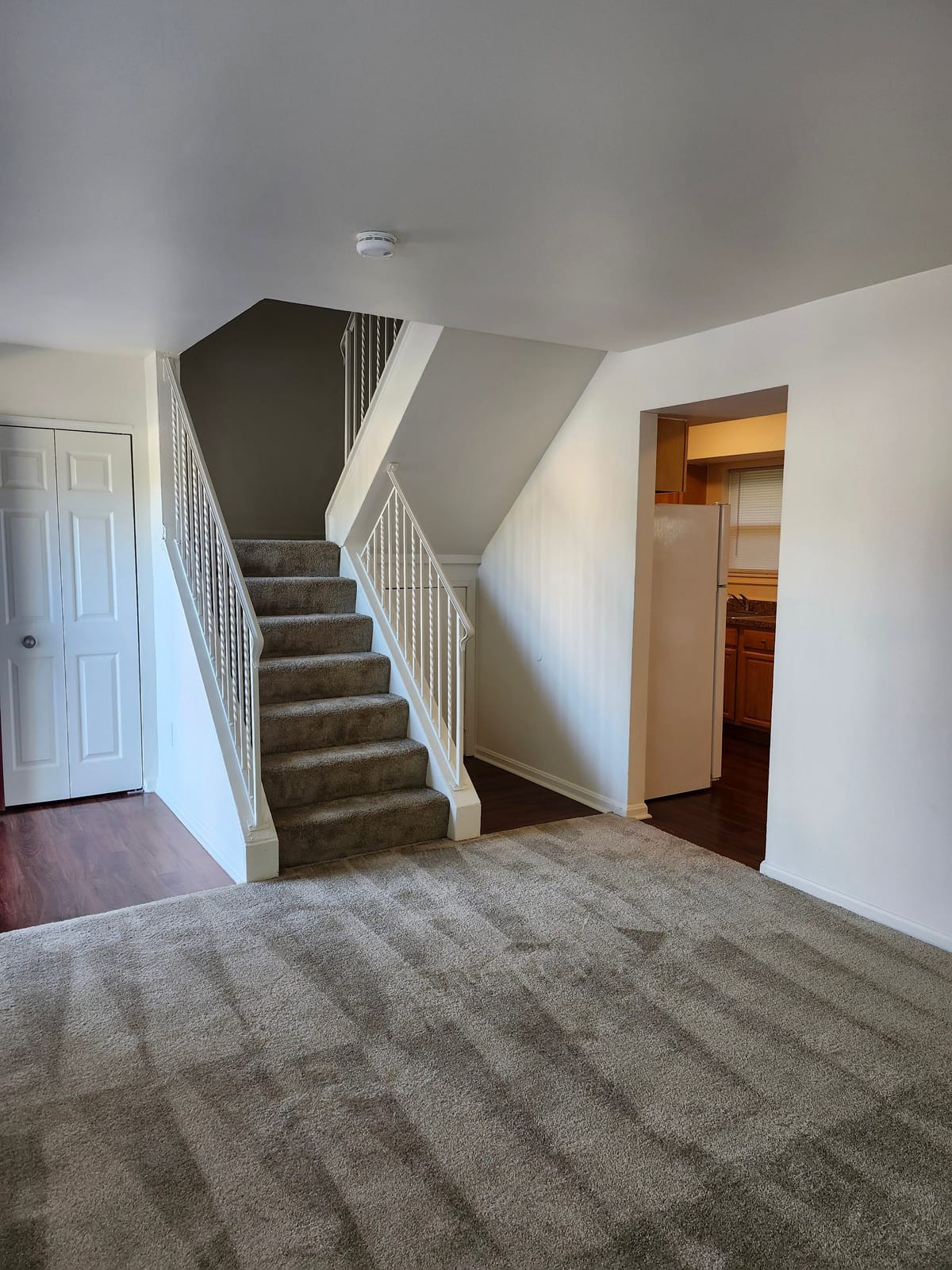 A carpeted living room at Calvertowne with a carpeted staircase, a closet with white doors, and a doorway through to the kitchen